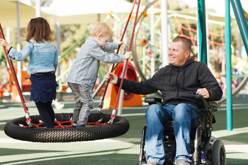 disabled father plays with children at inclusive playground